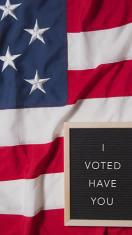 Vertical-Video-Of-Animated-Sign-Spelling-Out-I-Voted-Have-You-Lying-On-US-Stars-And-Stripes-Flag-For-American-Election-2024